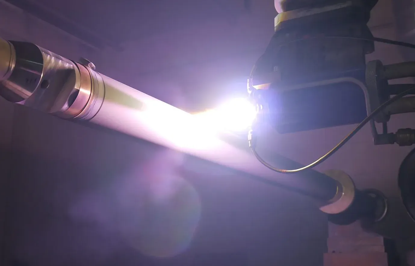 Bright flash during carbide coating. The machine applies the coating to an elongated component. Deutsch: Helles Licht während der Beschichtung mit Carbid. Die Maschine trägt die Beschichtung auf ein längliches Bauteil auf.